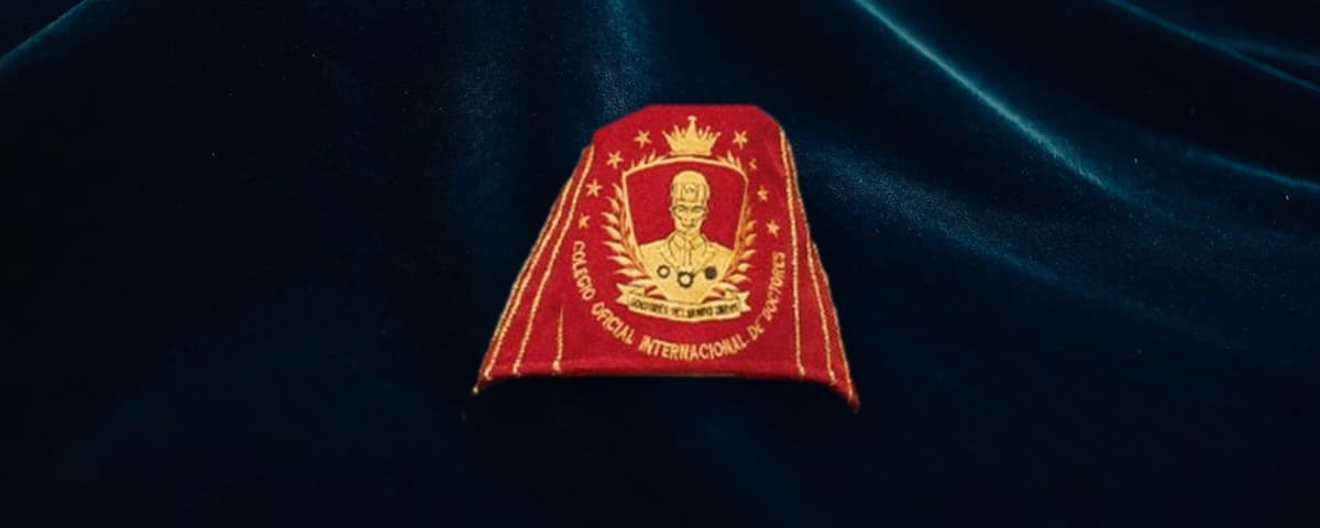 Birrete rojo de la colegiatura Honoris Causa, con el escudo del colegio bordado