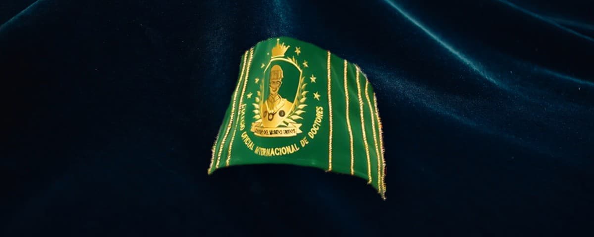 Birrete verde de la colegiatura de Doctor en Filosofía PhD, con el escudo del colegio bordado